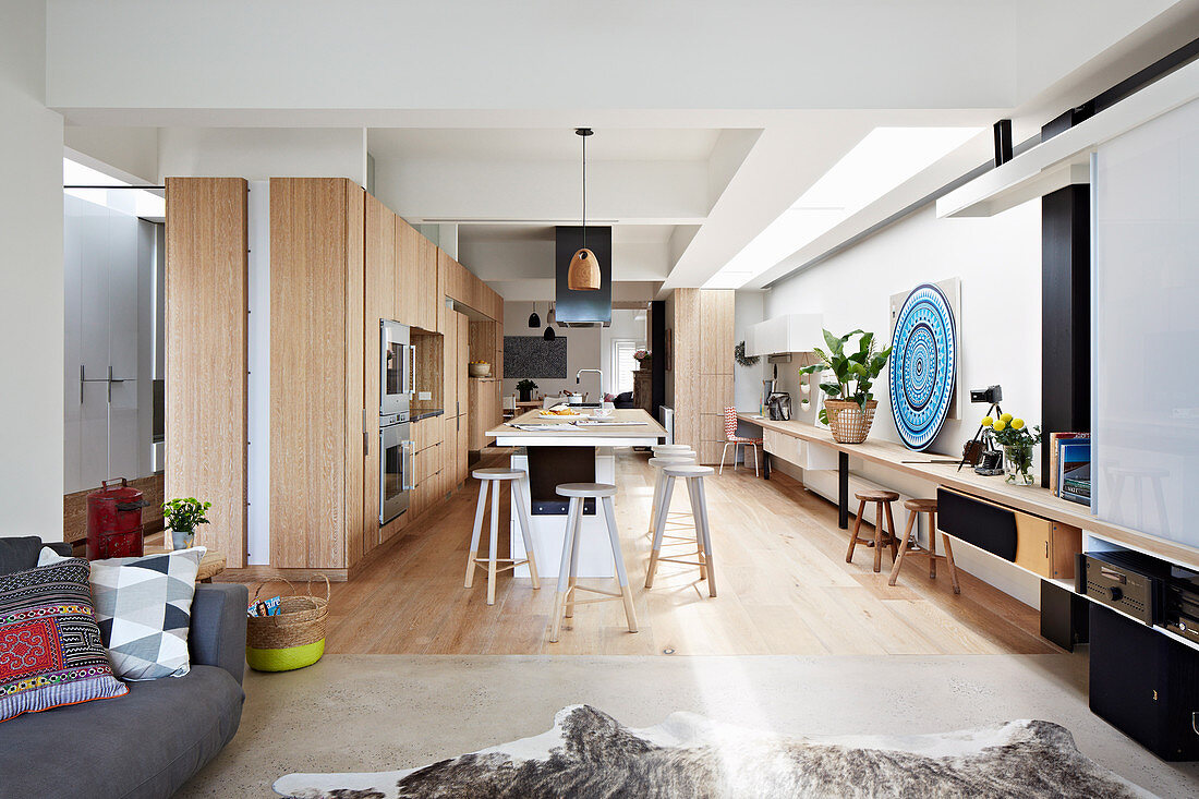 Fitted kitchen with wooden fronts and island, continuous wooden plate as a desk in an open living room