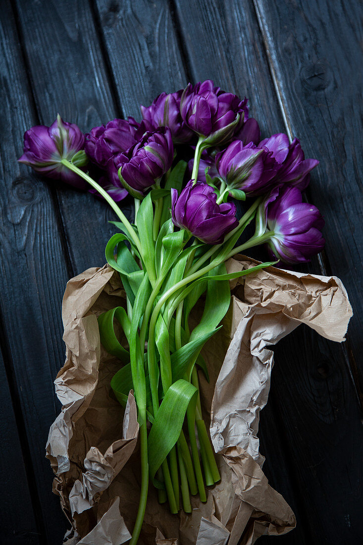 Lila Tulpen 'Purple Peony' mit Packpapier auf Holzuntergrund