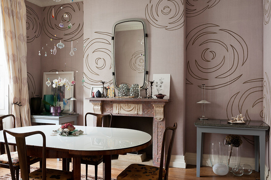 Wohnraum mit Esstisch und Kamin vor altrosafarbener Wandtapete mit Blütenmotiv