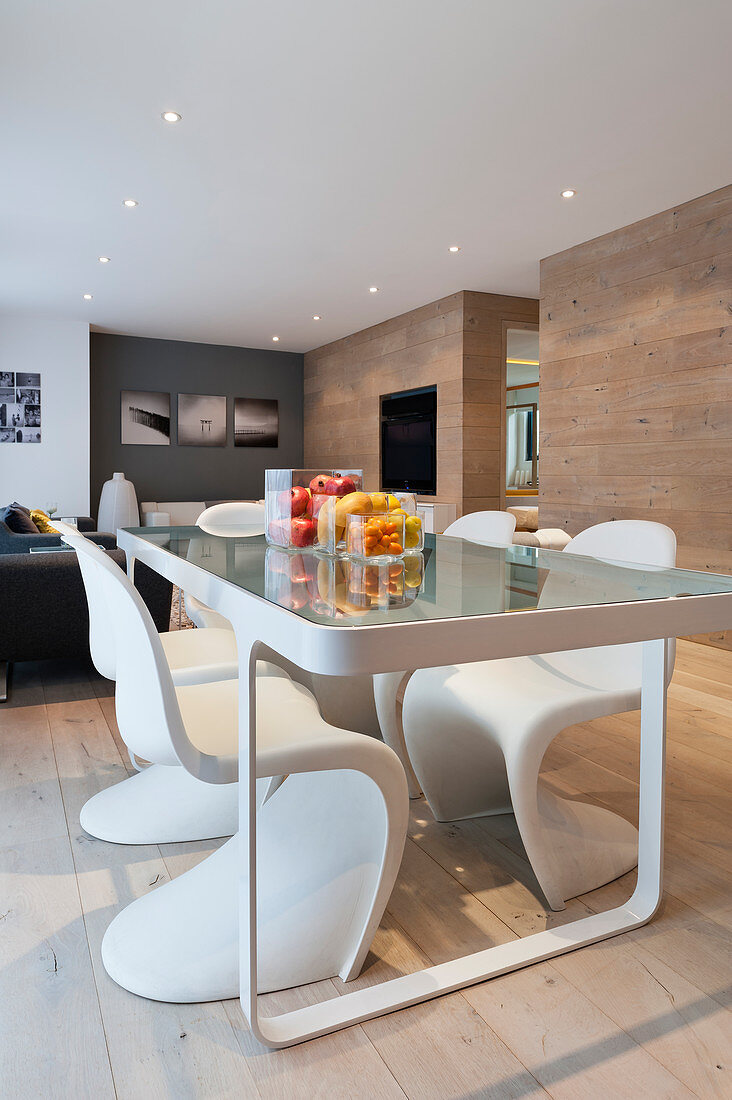 Glas-Esstisch mit Designerstühlen in modernem Wohnraum mit Eichenholzwandverkleidung