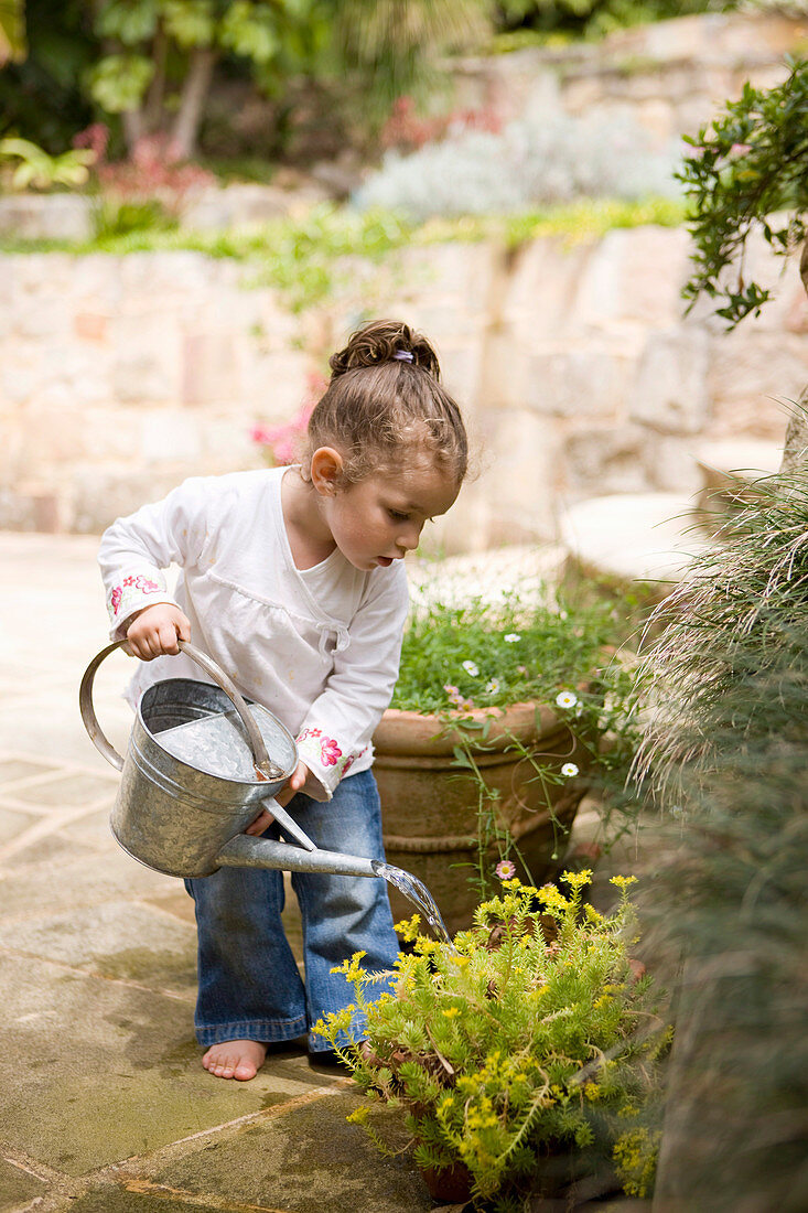 Kleines Mädchen gießt mit Gießkanne Pflanzen auf Steinterrasse