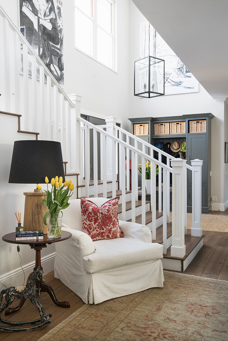 White, loose-covered armchair and side table next to foot of staircase