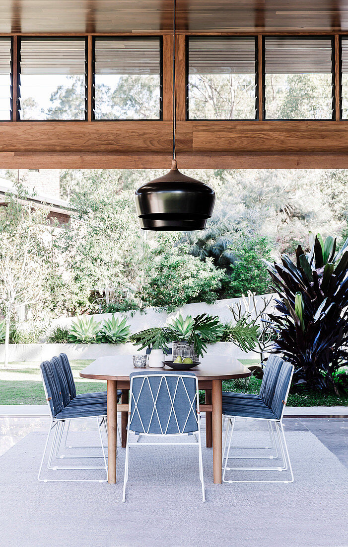 Esstisch aus Holz mit filigranen Metallstühlen vor Terrasse