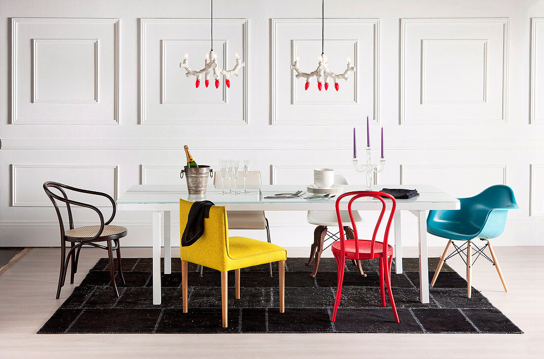 White dining table with various colorful chairs against white wall