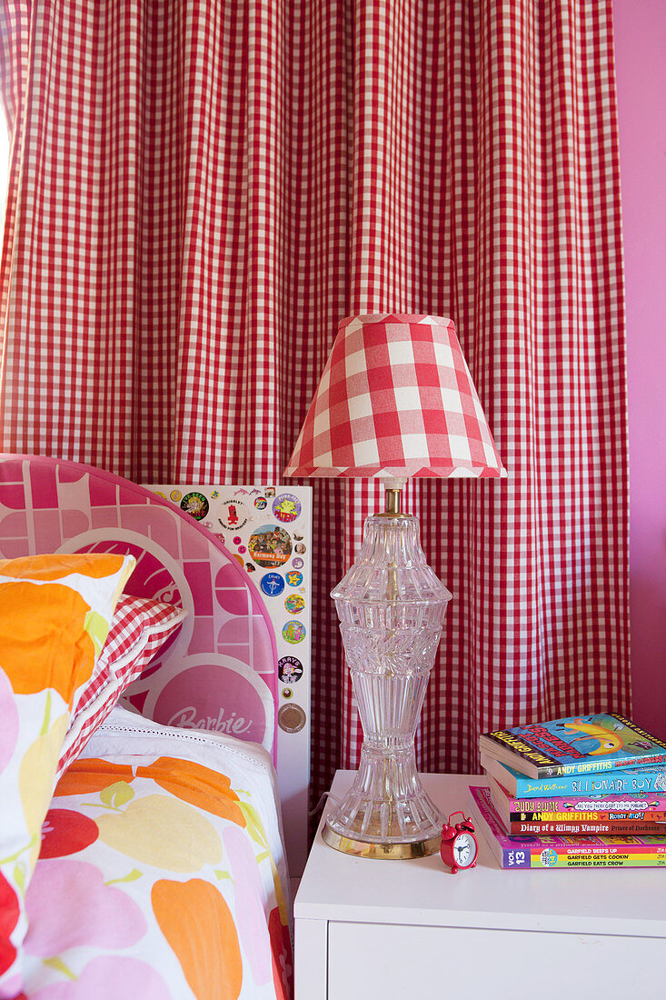 Bunte Bettwäsche, Nachttisch und Tischlampe vor rot-weiß kariertem Vorhang im Mädchenzimmer