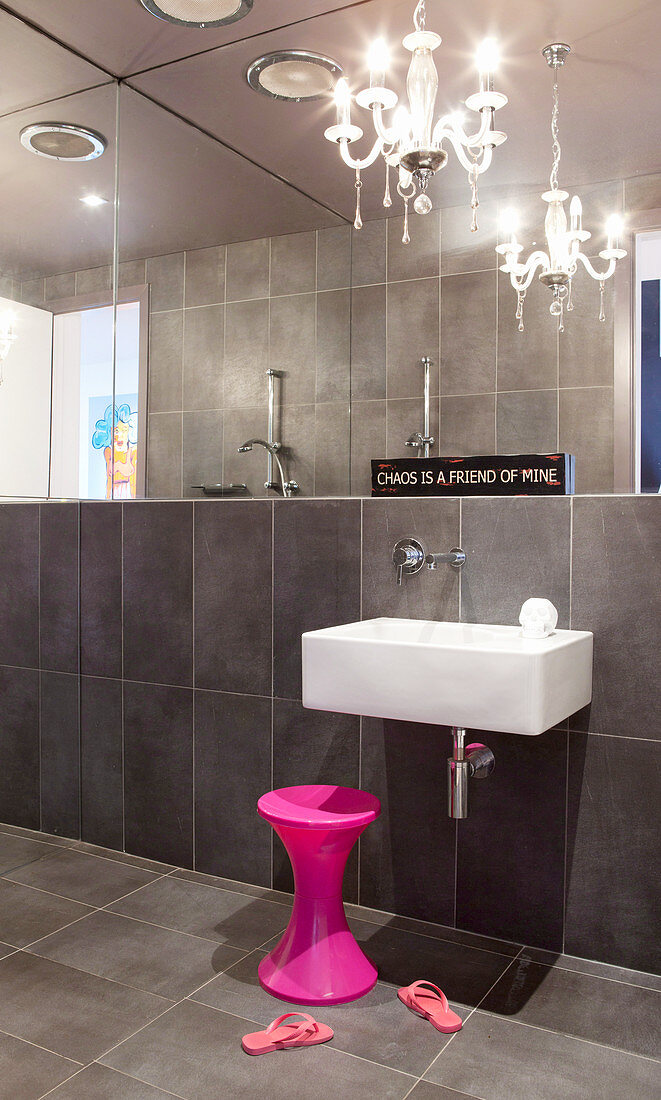 Sinks, pink stools and chandeliers in the bathroom with dark tiles