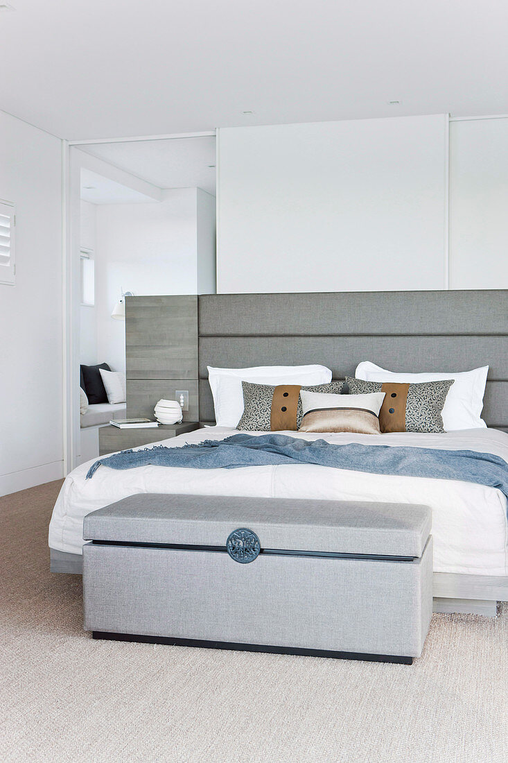 Upholstered chest in front of the bed in the elegant bedroom in white and gray
