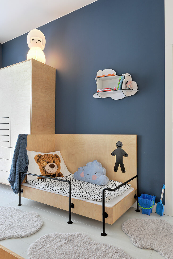 Bett und Kleiderschrank aus Sperrholz an blauer Wand im Kinderzimmer