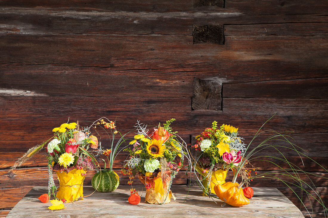 Blumensträuße in mit Herbstlaub umhüllten Vasen und Zierkürbisse mit Gräsern