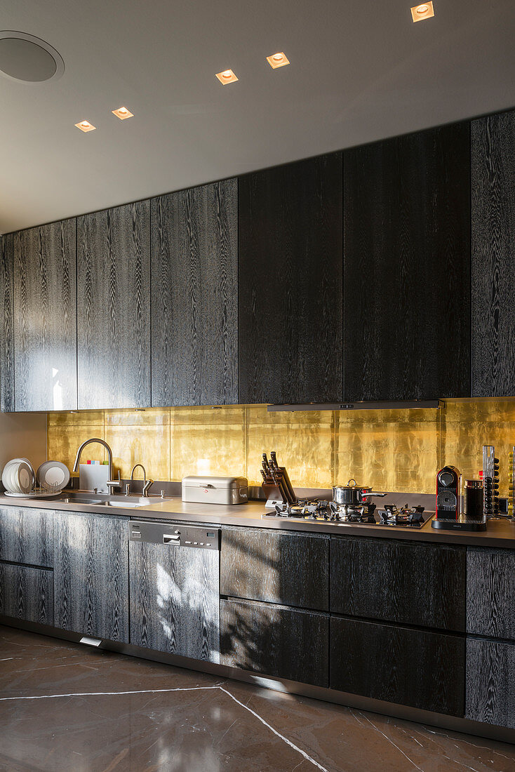 Black wooden cabinets and golden splashback in kitchen