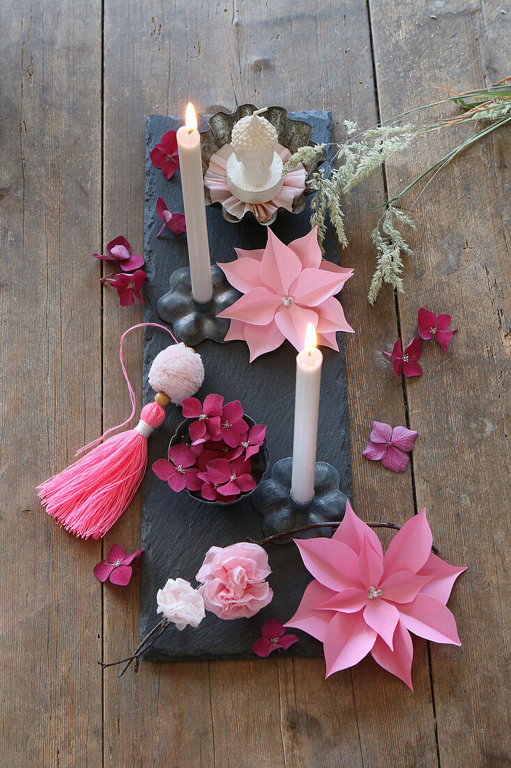 Arrangement of paper flowers and grey candles on slate board decorating tablw