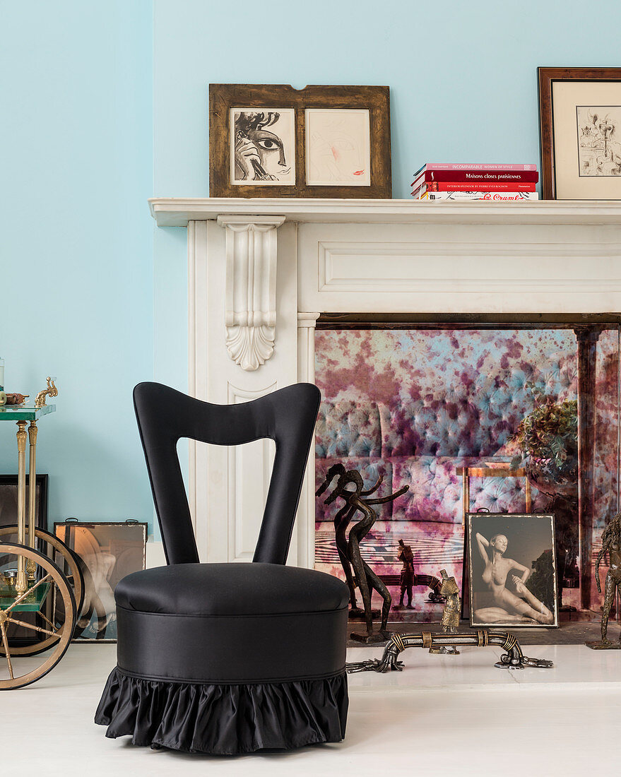 Black easy chair in front of marble fireplace decorated with pictures and sculptures