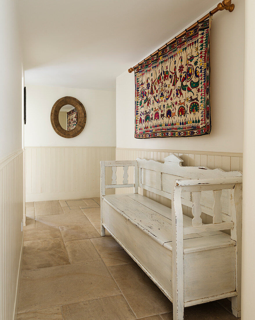 Folkloristischer Wandteppich über weißer Holzbank im Flur