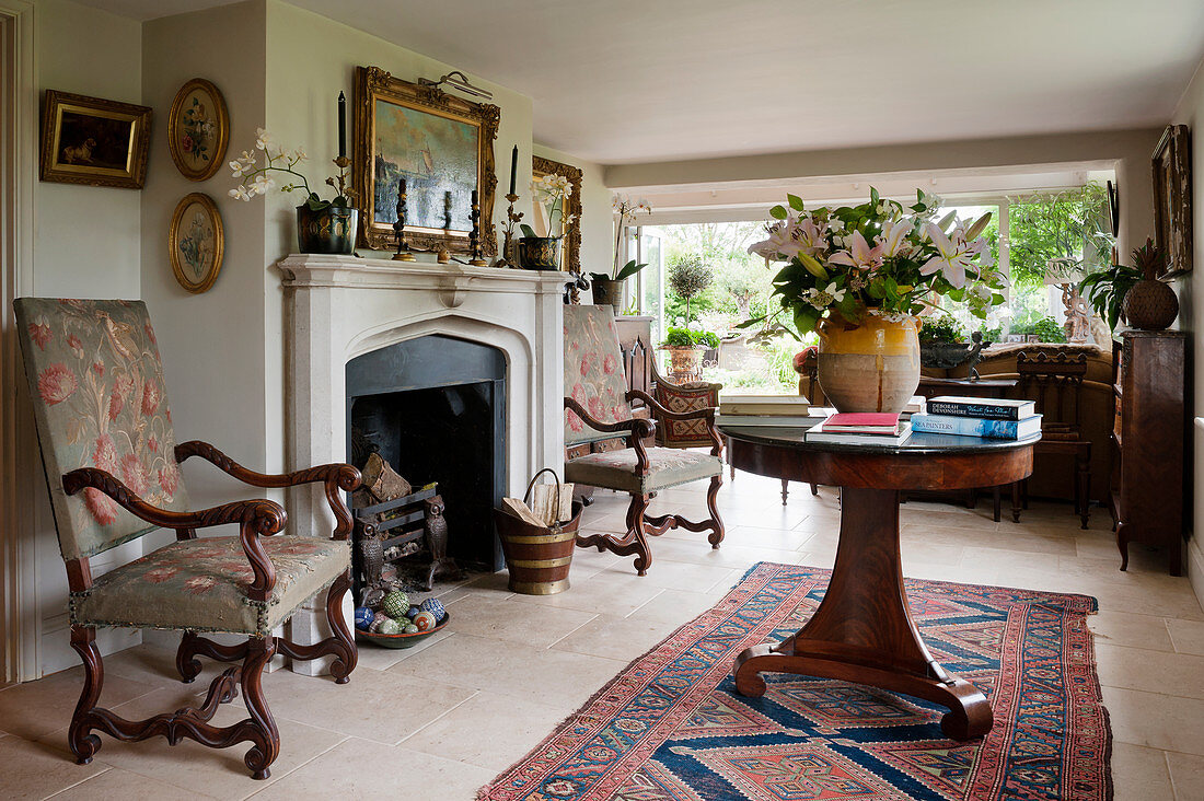Antique armchairs and round table in front of fireplace in interior of renovated English country house