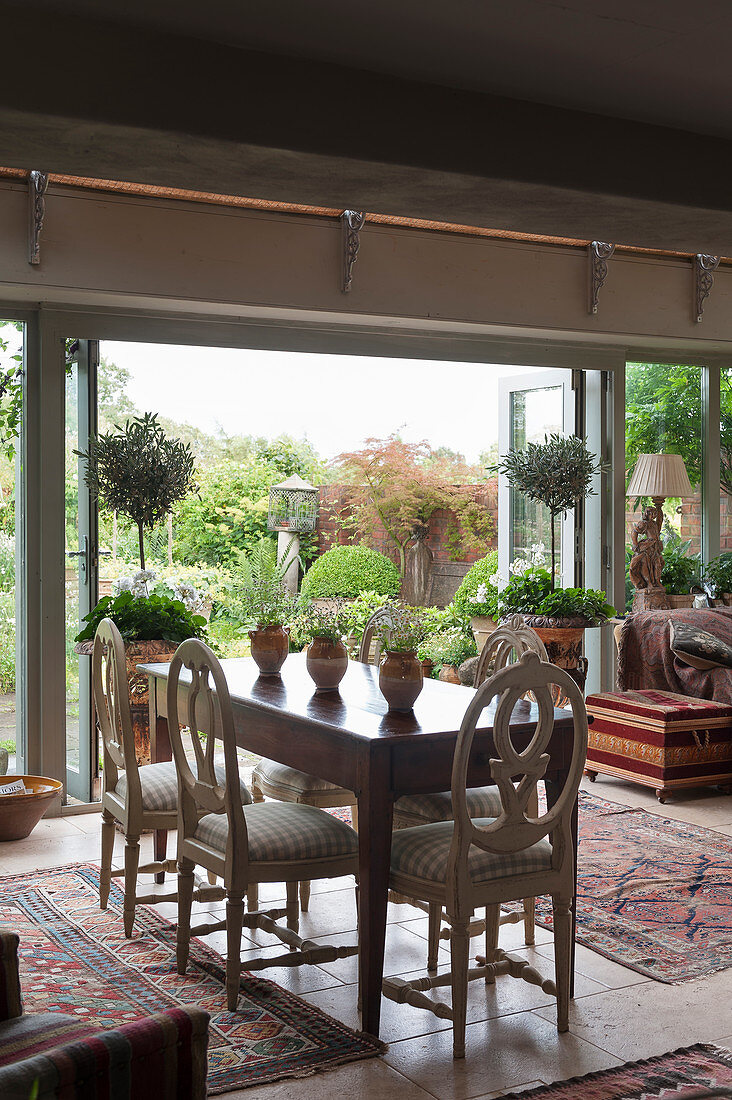 Dining table and antique chairs in front of open terrace doors in English country house
