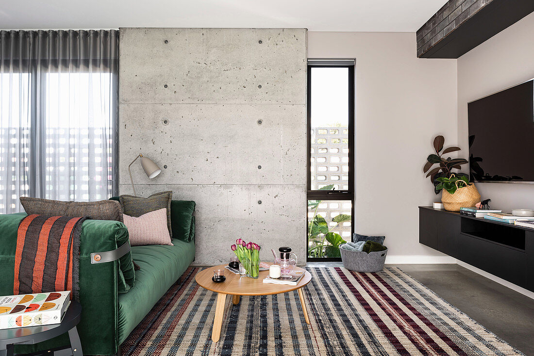 Green velvet sofa in front of concrete wall in modern living room