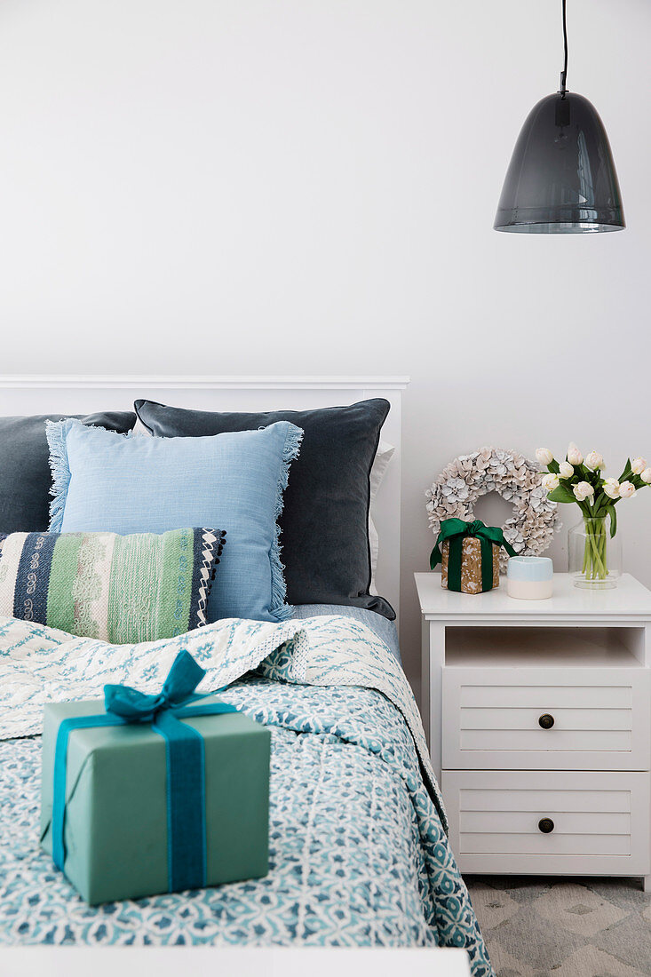 Geschenk auf Bett mit Tagesdecke und Kissen in Blautönen