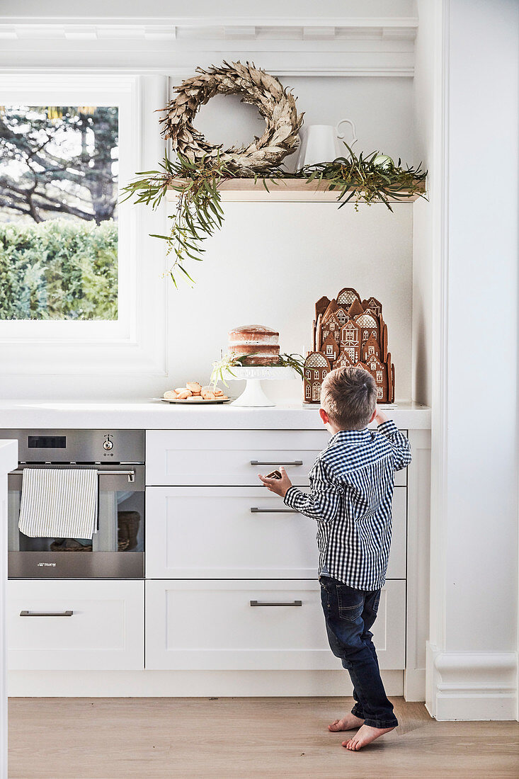 Winterlicher Dekokranz auf Küchenregal darunter kleiner Junge vor Lebkuchenhaus