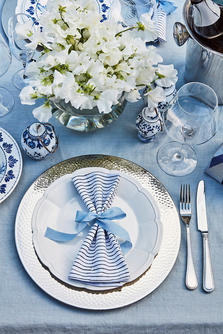 Festive table setting with silver place plate, blue-striped napkin and bouquet