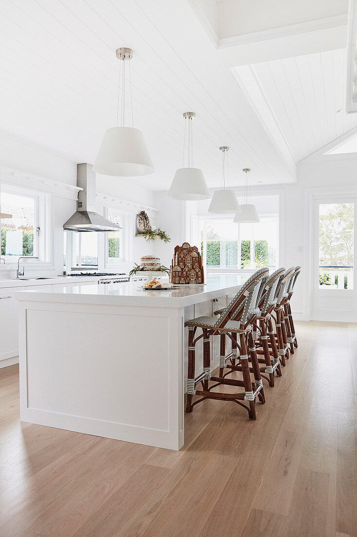 Bright white kitchen with bar chairs lined up on a spacious kitchen island