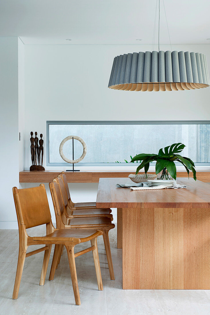 Designerlampe über Esstisch mit Holzsstühlen neben Fensterband