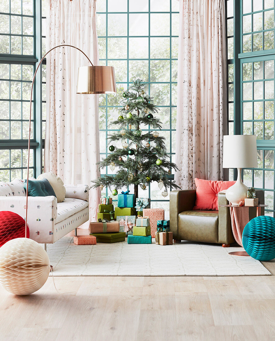 Wrapped gifts under Christmas tree, sofa and armchair in living room with glass walls