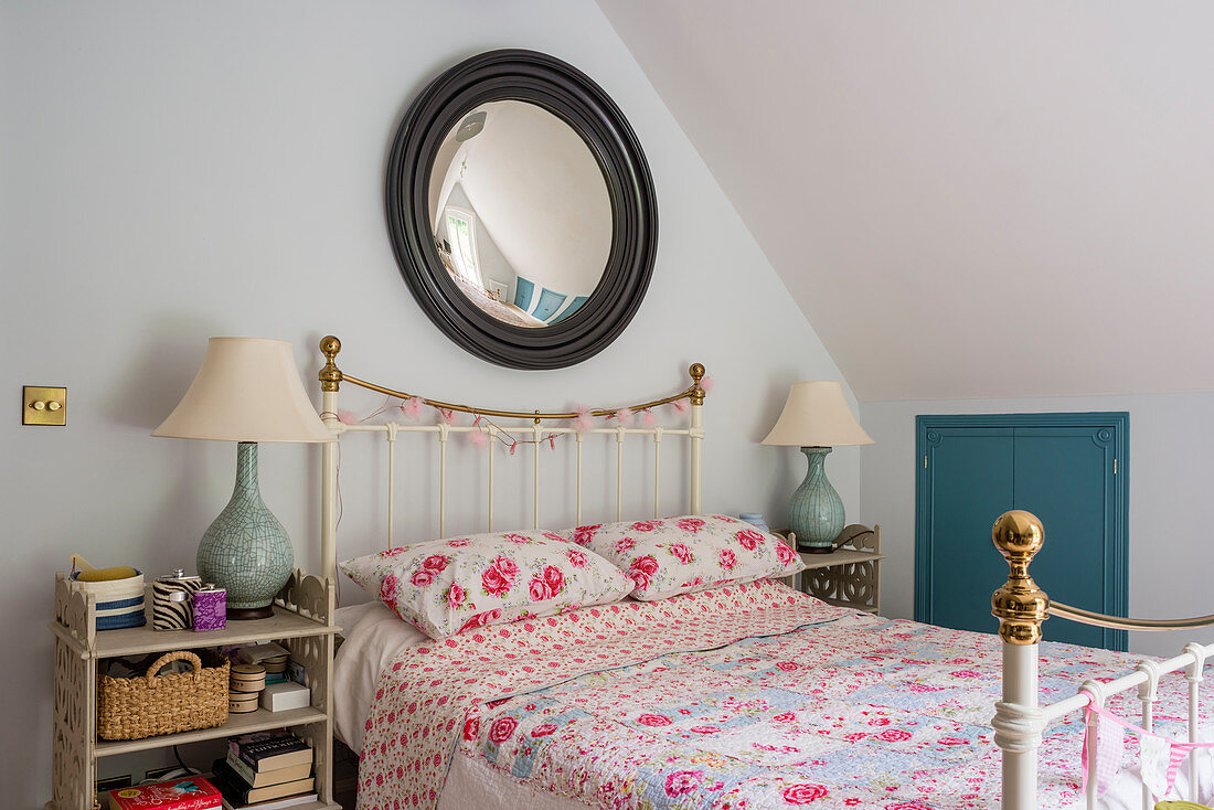 Fisheye mirror above metal bed with rose-patterned quilt