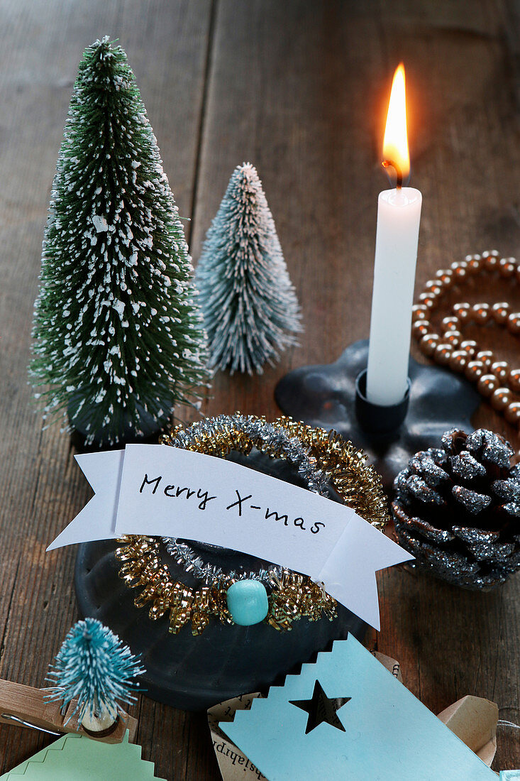 Kleine Tannenbäumchen, brennende Kerze und Xmas-Schild