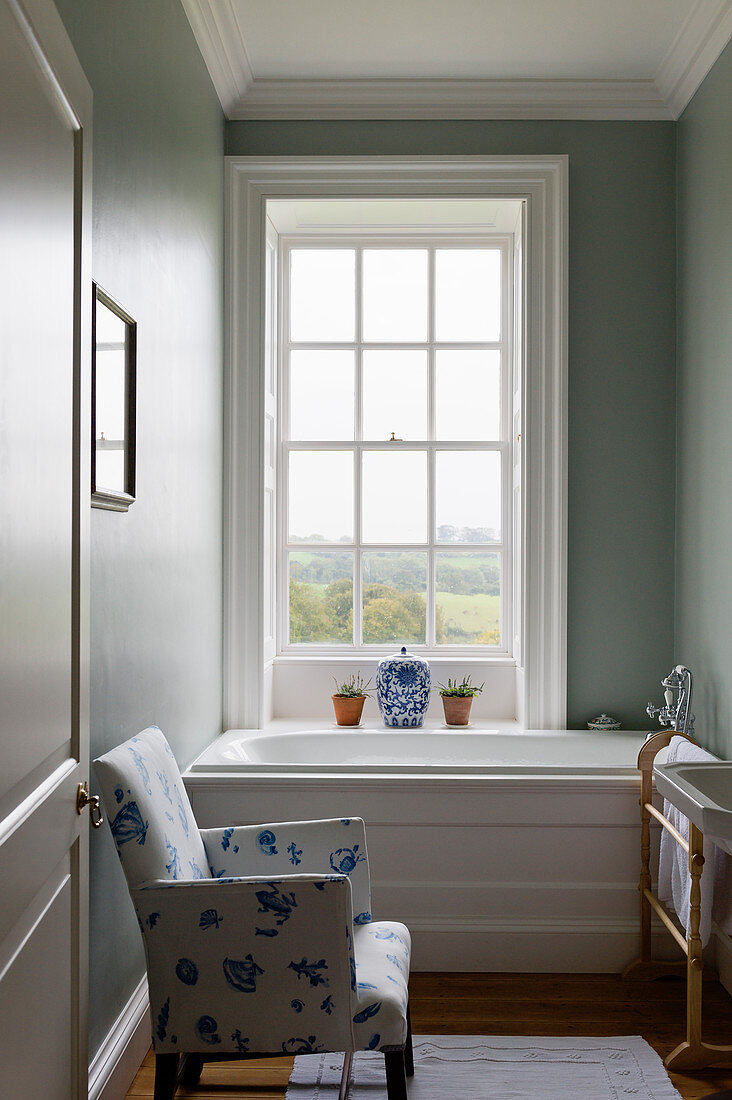 White-and-blue armchair next to bathtub below lattice window