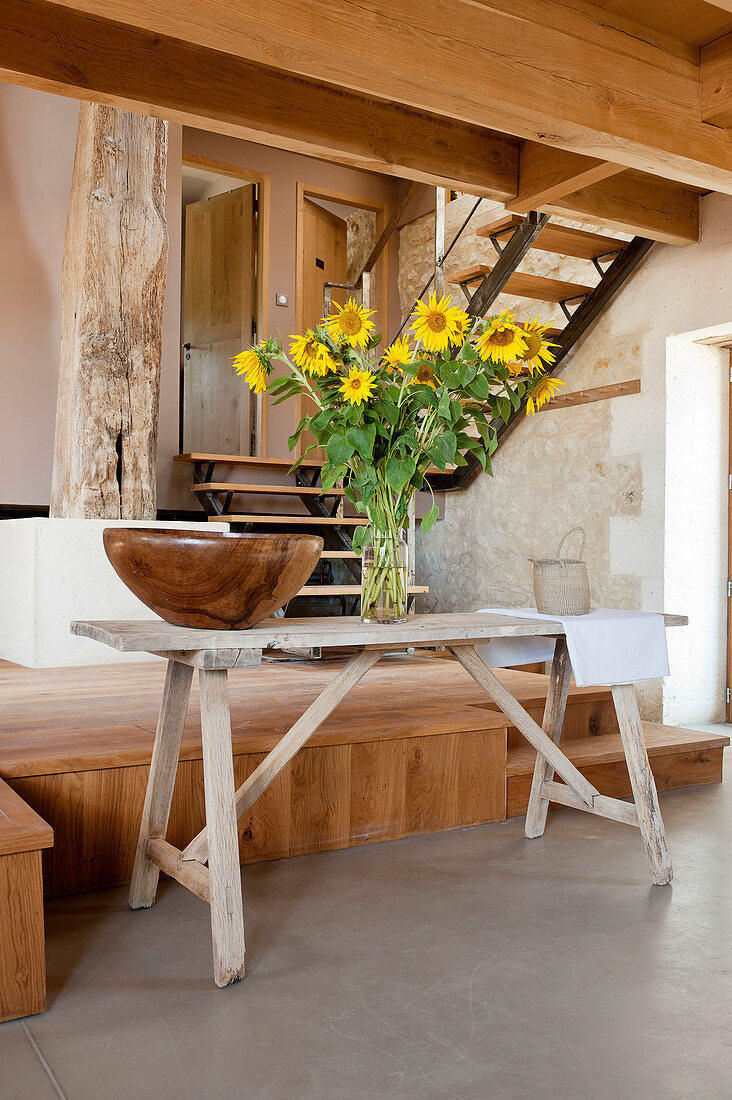 Holzschale und Sonnenblumenstrauß auf Tisch in umgebauter Scheune