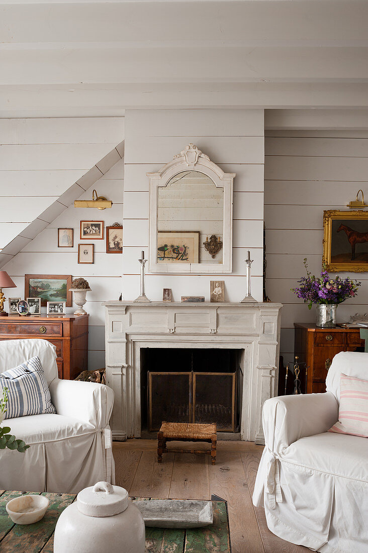 Weiße Hussensessel vor Kamin im Wohnzimmer mit weiß gestrichenen Holzwänden