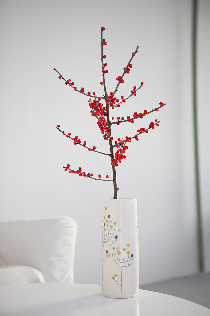Dekorativer Zweig mit roten Beeren in Vase auf Tisch
