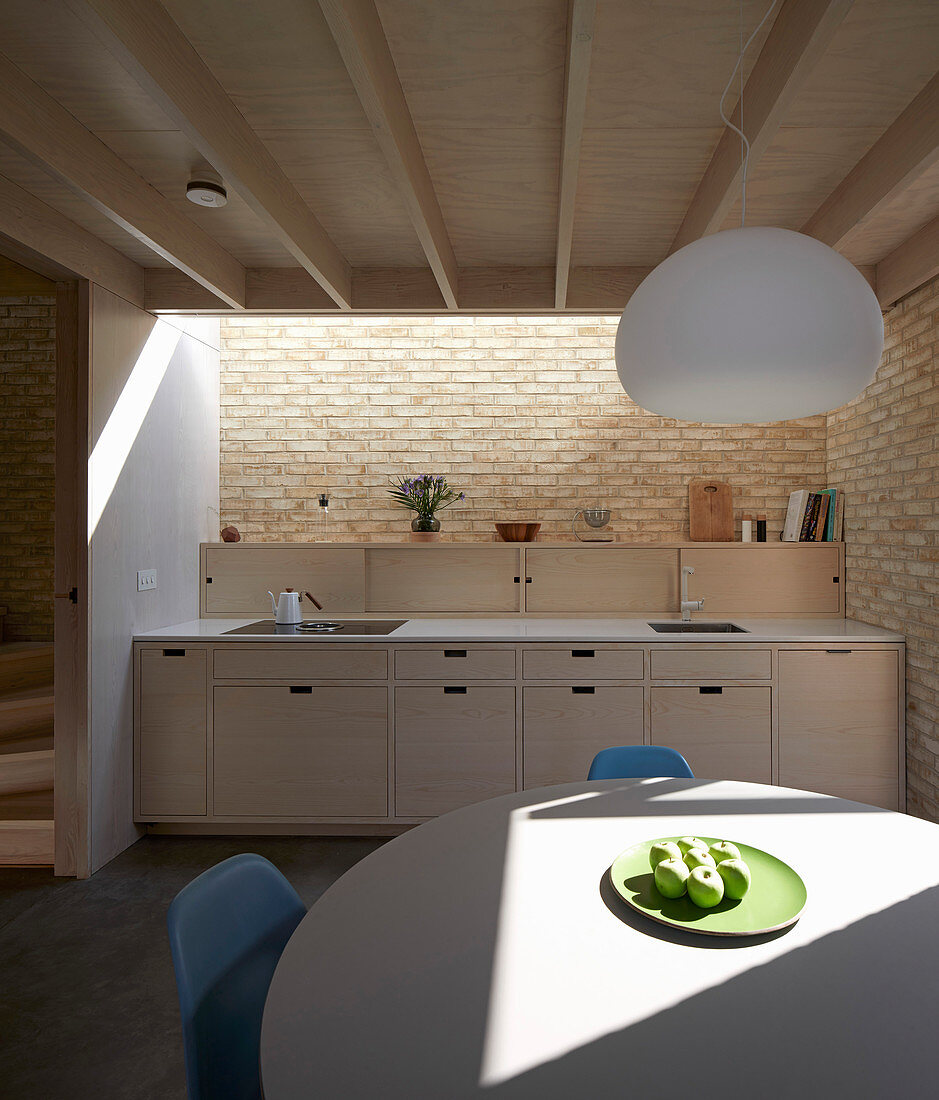 Runder Tisch in offener, moderner Küche mit Küchenzeile, Ziegelwand und Oberlicht