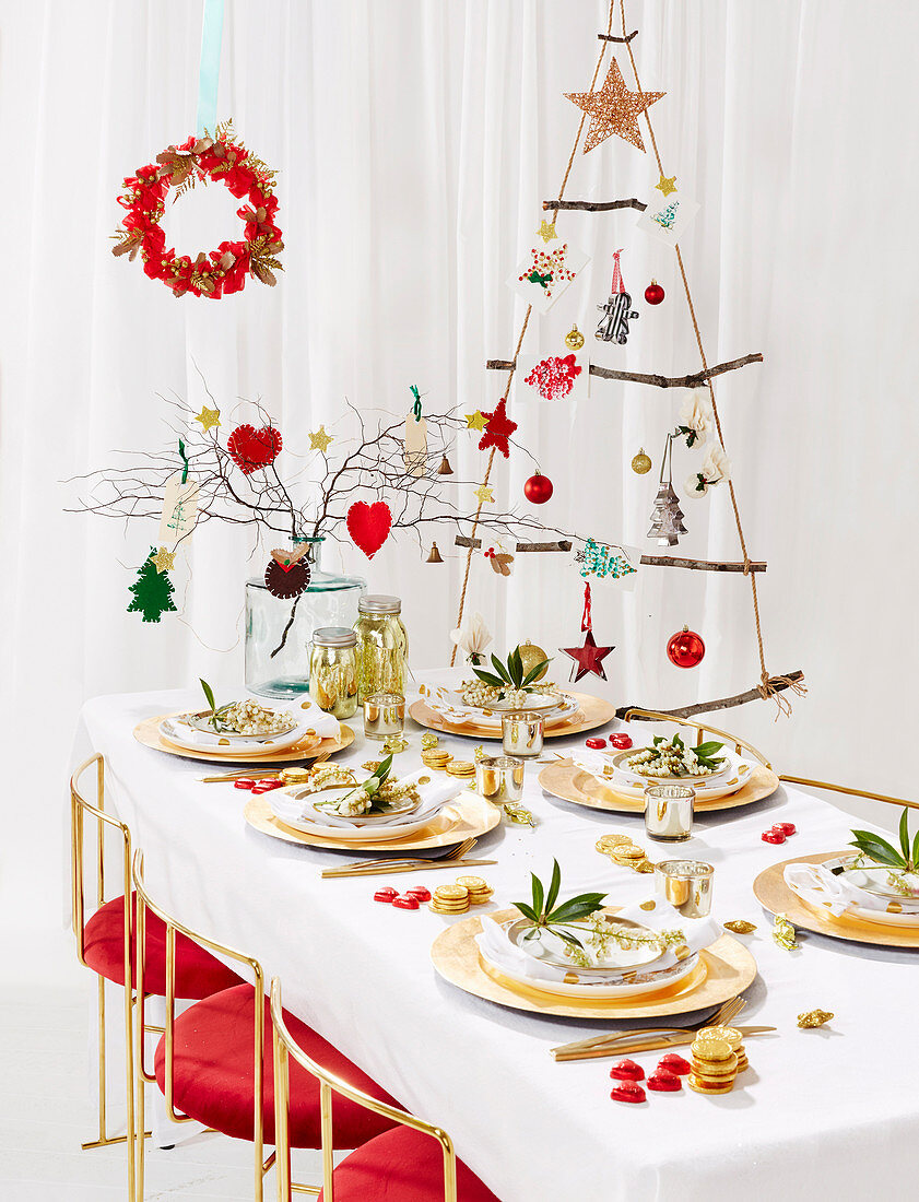 Gedeckter Weihnachtstisch vor hängendem DIY-Weihnachtsbaum aus Seil und Ästen