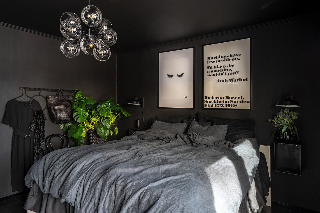 Doppelbett mit grauer Bettwäsche im Schlafzimmer mit schwarzen Wänden