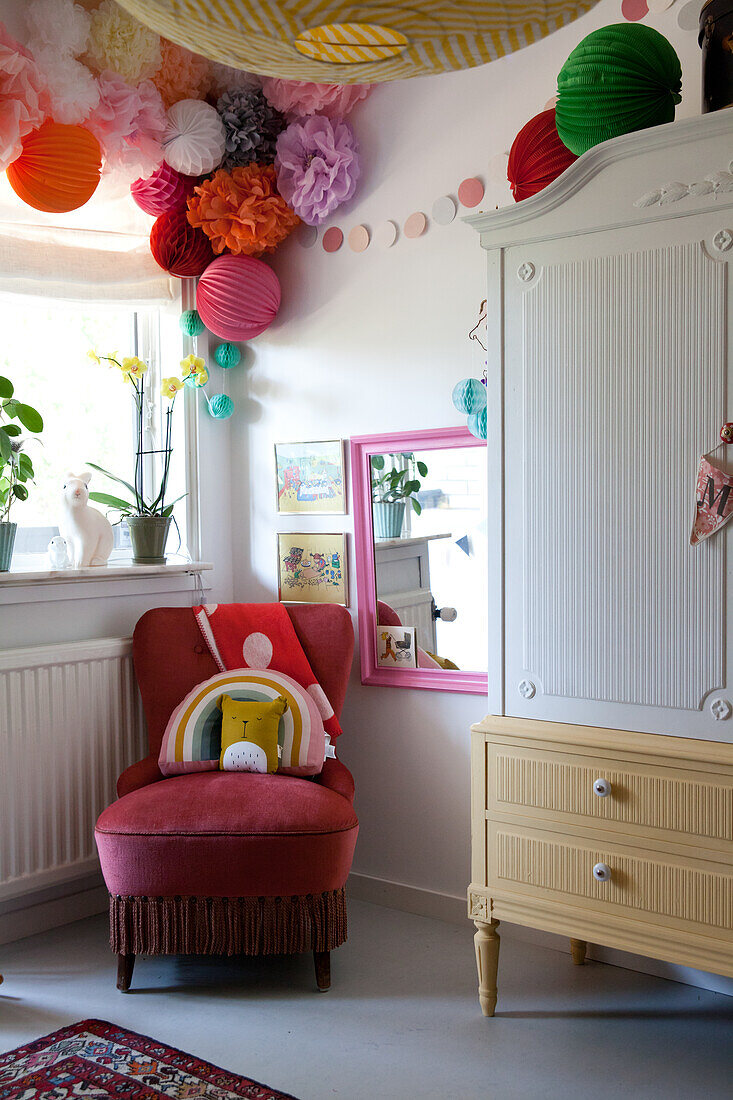 Old, red velvet chair below arrangement of pompoms in child's bedroom