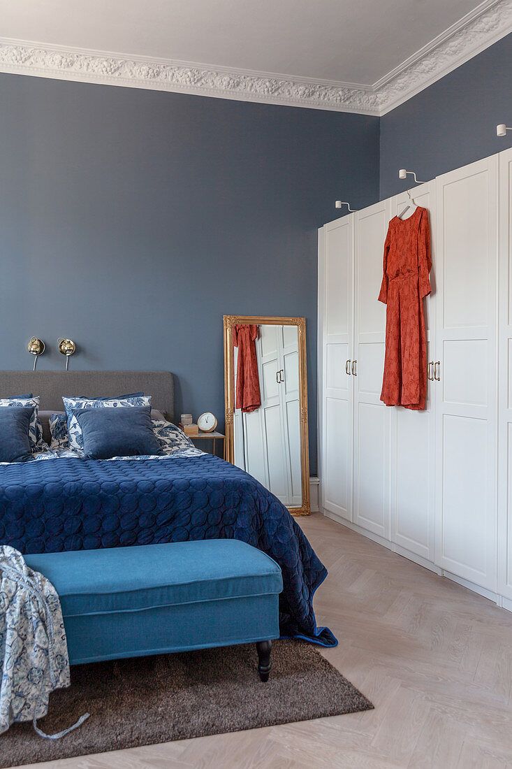 Blue velvet throw on bed and bedroom bench next to white modern wardrobe