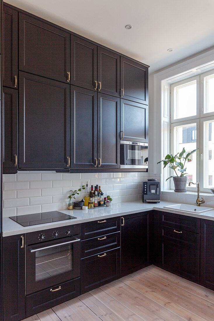 Base units and tall wall units with black fronts and splashback of white subway tiles in fitted kitchen