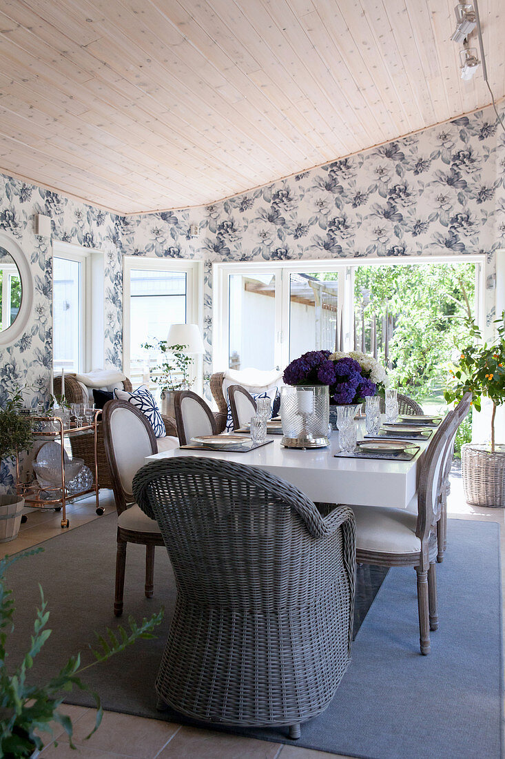 Wicker chair and upholstered chairs in dining room with floral wallpaper