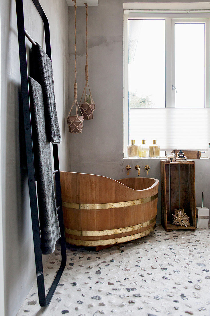 Free-standing wooden bathtub on stone floor of bathroom