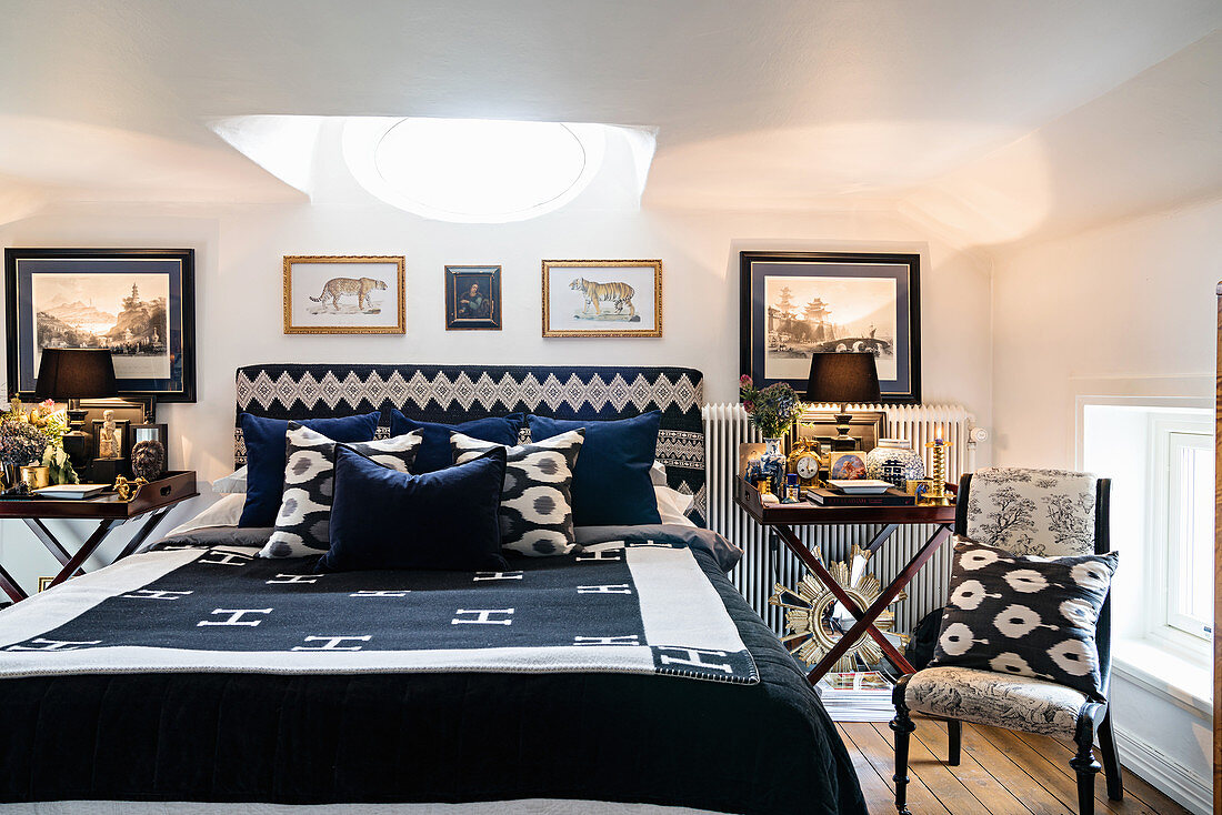 Üppig dekorierte Nachttische neben blau-weißem Bett in Schlafzimmer mit ovalem Oberlichtfenster