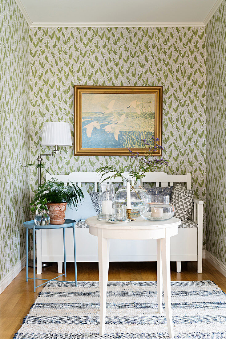 Bench, houseplant, lamp and painting on floral wallpaper in niche