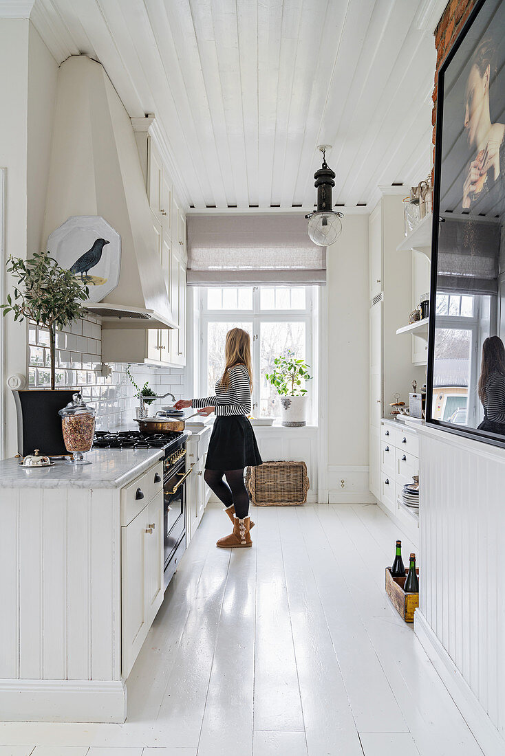 Helle Küche mit weißem Dielenboden, Frau im Hintergrund