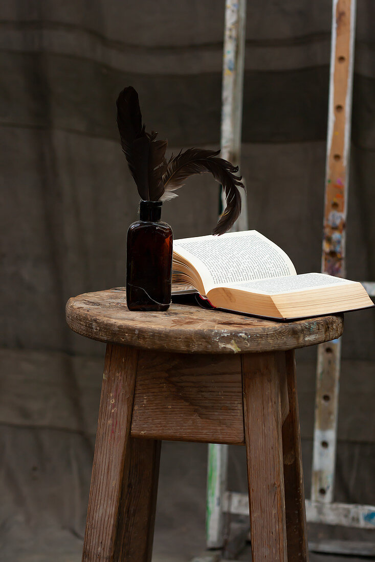 Open book and feathers in bottle on wooden stool