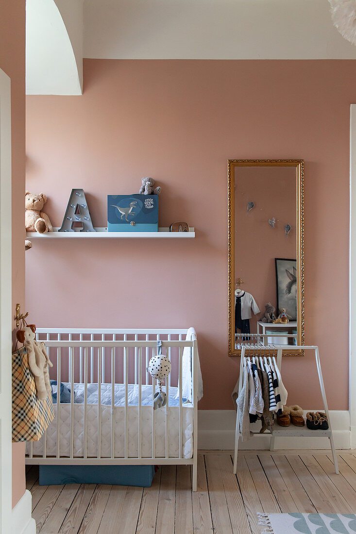 Cot and small clothes rack in nursery with pink wall