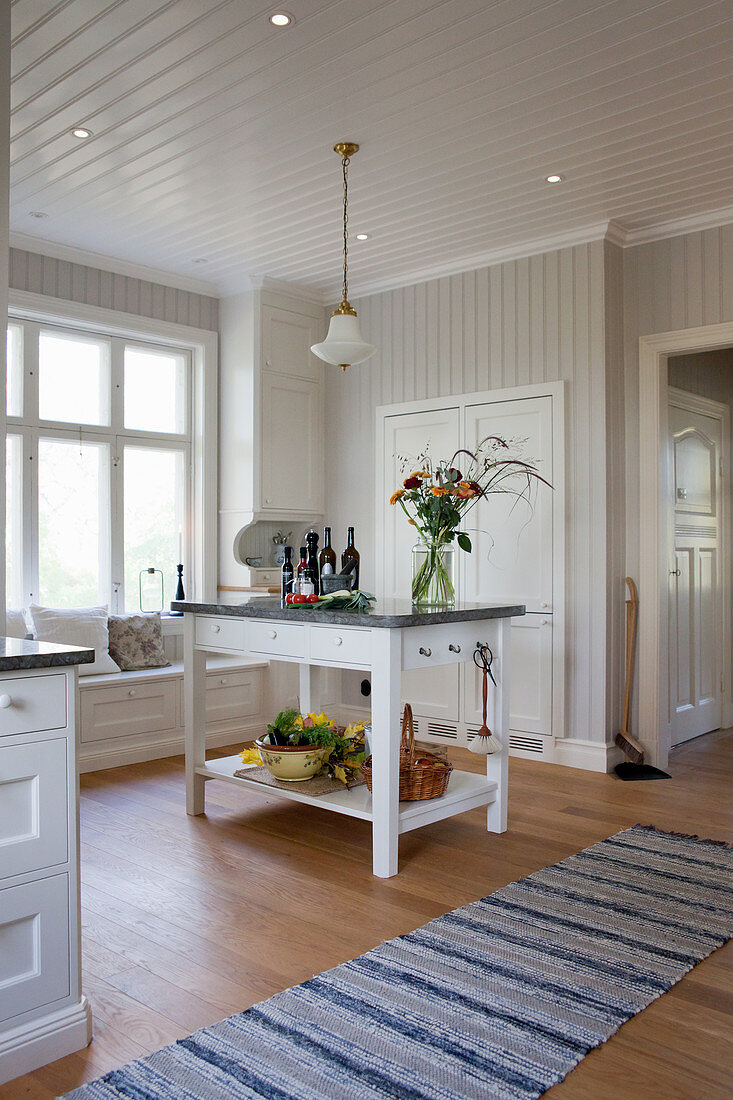 Kücheninsel in geräumiger weißer Landhausküche mit Sitzbank vorm Fenster