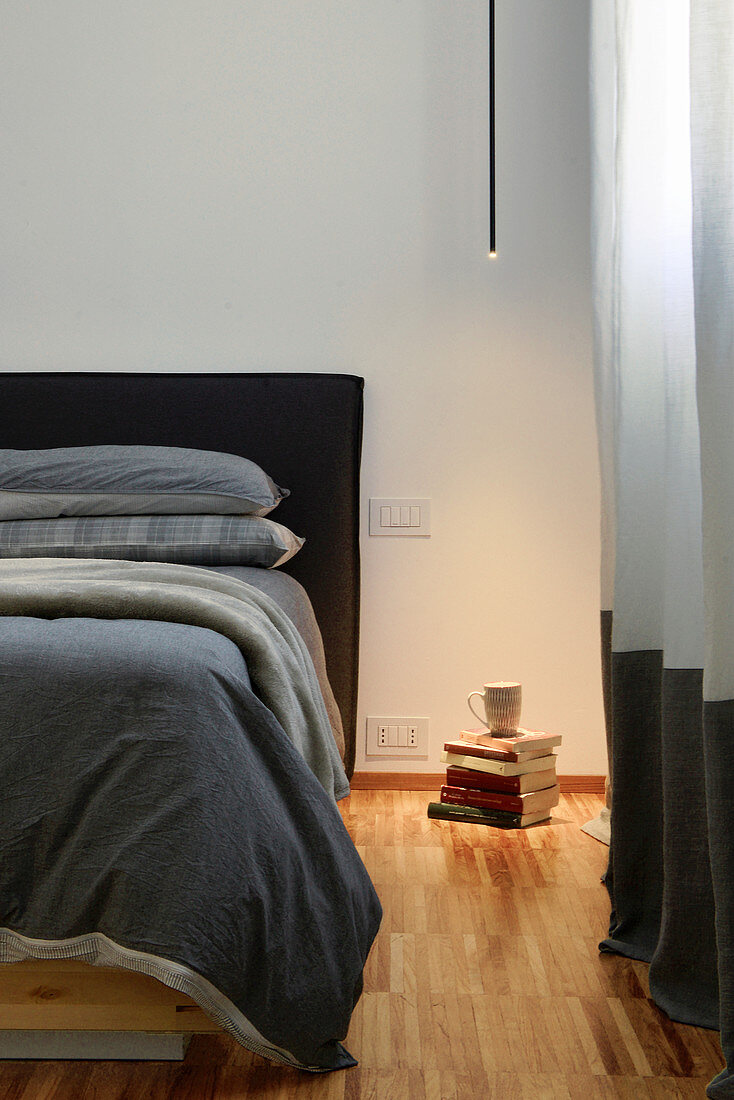 Minimalist ceiling light illuminating stack of books next to bed