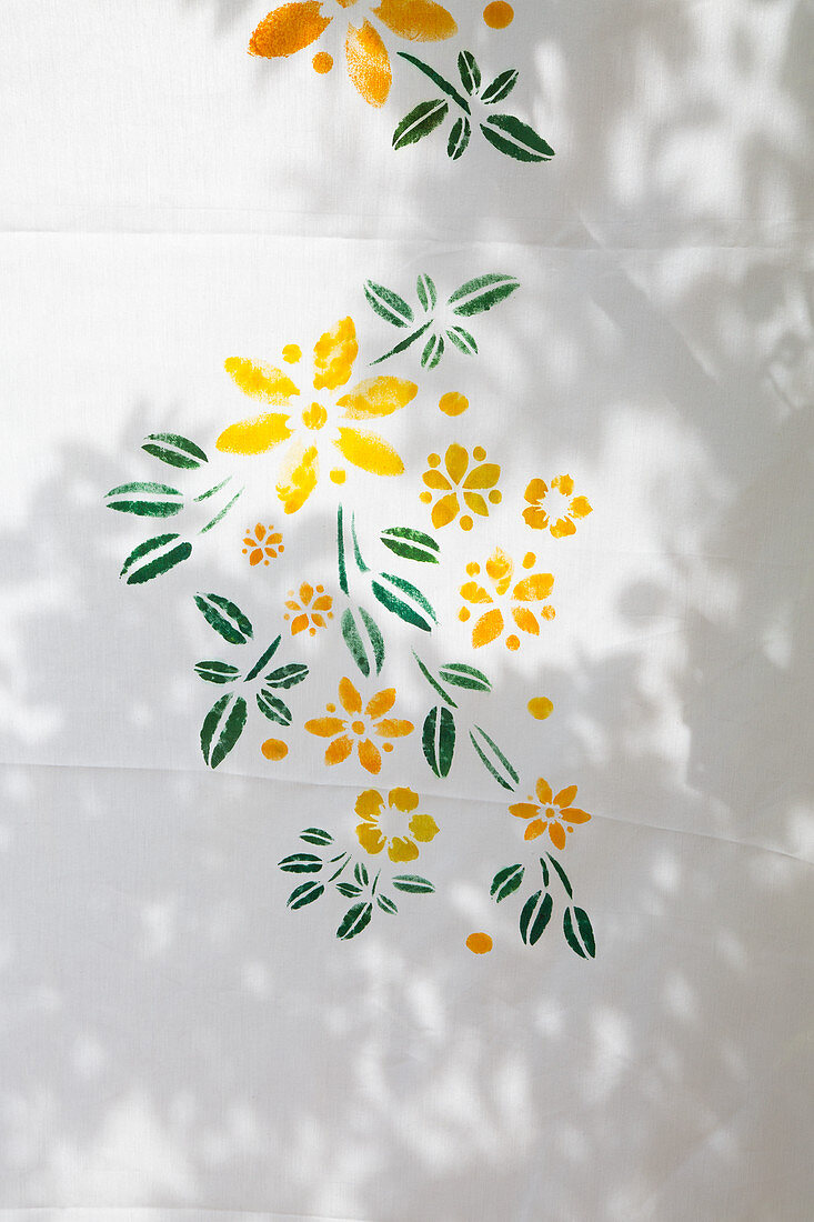 Gelbe Blumen und grüne Blätter auf weißen Stoff gemalt