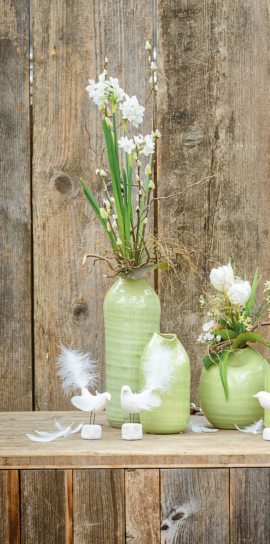 Grüne Vasen mit Frühlingssträußen vor rustikaler Holzwand