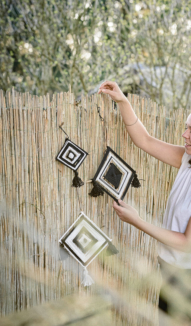 Woman hanging woollen mobile on screen fence